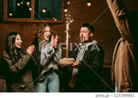 Friends celebrating a birthday with a cake and fireworks indoors at night 125289981