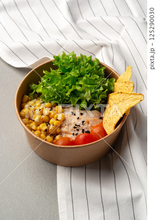 Healthy lunch bowl featuring corn, lettuce, and tortilla chips on a gray table with a striped cloth backdrop Healthy lunch bowl featuring corn, lettuce, and tortilla chips on a gray table with a striped cloth backdrop 125290030