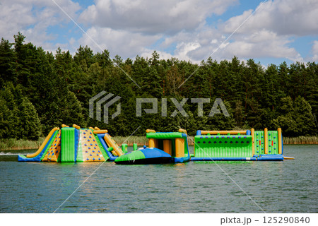 Inflatable obstacle course on lake with forest backdrop for summer fun. Weekend concept near the forest and lake 125290840