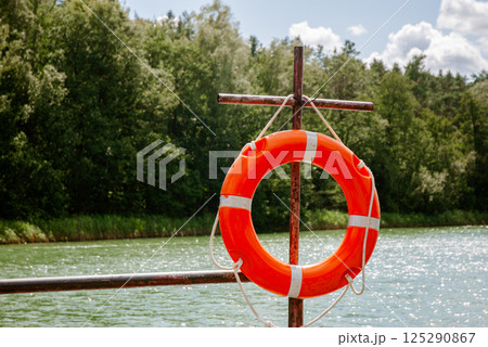 Bright orange lifebuoy on lakeside dock against forest and sky scene. Weekend concept near the forest and lake Bright orange lifebuoy on lakeside dock against forest and sky scene. Weekend concept near the forest and lake 125290867