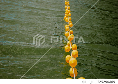 Yellow buoys floating on lake water surface for nautical safety and boundary marking. Weekend concept near the forest and lake Yellow buoys floating on lake water surface for nautical safety and boundary marking. Weekend concept near the forest and lake 125290869