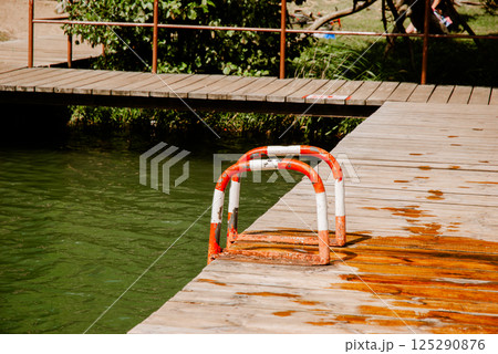 Tranquil lakeside scene with wooden dock and ladder on a sunny day. Weekend concept near the forest and lake Tranquil lakeside scene with wooden dock and ladder on a sunny day. Weekend concept near the forest and lake 125290876