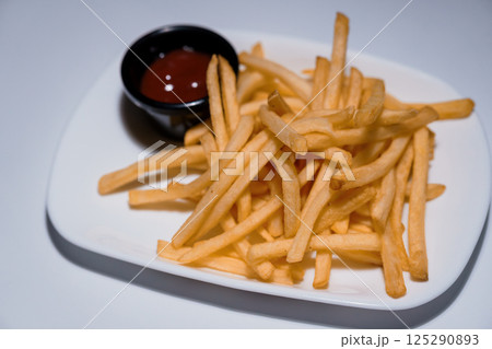 Golden french fries served on a white rectangular plate with small bowl of red ketchup sauce, studio shot isolated on light background 125290893