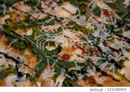Close-up of gourmet pizza with mozzarella, arugula, balsamic glaze and parmesan cheese on a rustic crust, appetizing food photography 125290903