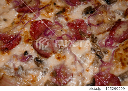 Close-up view of a delicious pizza with pepperoni, red onion slices, mushrooms and melted cheese on a golden brown crust 125290909