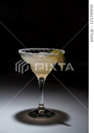 Classic margarita cocktail in a salt-rimmed glass with a lime garnish, presented against a dark dramatic background Classic margarita cocktail in a salt-rimmed glass with a lime garnish, presented against a dark dramatic background 125290950