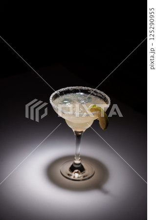 Classic margarita cocktail in a salt-rimmed glass, garnished with lime slice against dark background, perfect for bar or restaurant promotions 125290955