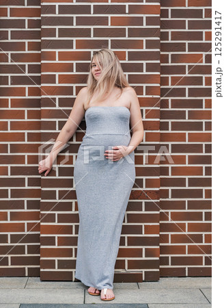 Beautiful pregnant woman posing against a brick wall while touching her belly in natural light Beautiful pregnant woman posing against a brick wall while touching her belly in natural light 125291417