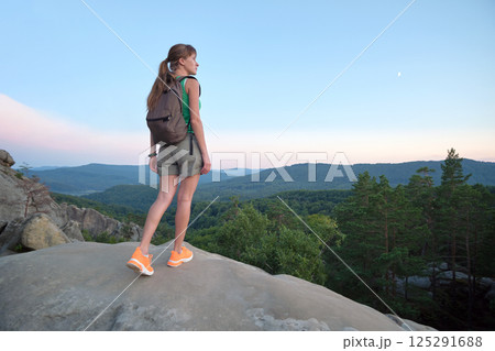Young woman hiking alone on mountain footpath. Female hiker enjoying view of evening nature on wilderness trail. Active way of life concept 125291688
