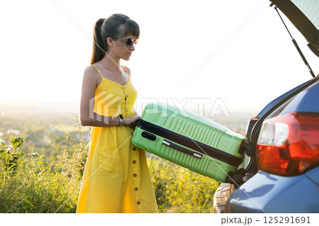 Young woman driver taking green suitcase out from car trunk. Travel and vacations concept. 125291691