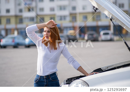 Young stressed woman driver standing near broked car with open hood. Young stressed woman driver standing near broked car with open hood. 125291697
