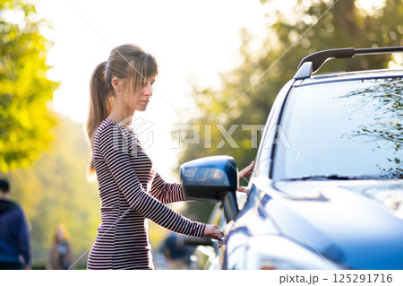 Young female driver resting near her car enjoying warm summer day. Travel and getaway concept. Young female driver resting near her car enjoying warm summer day. Travel and getaway concept. 125291716