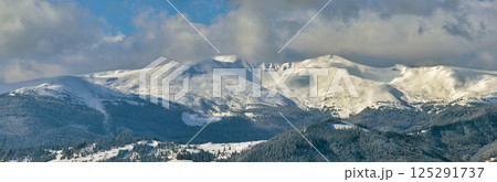 Winter landscape with high mountain hills covered with evergreen pine forest after heavy snowfall on cold wintry day. 125291737