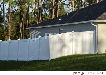 White vinyl picket fence on green lawn surrounding property grounds for backyard protection and privacy 125291751