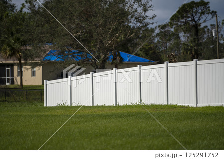White vinyl picket fence on green lawn surrounding property grounds for backyard protection and privacy White vinyl picket fence on green lawn surrounding property grounds for backyard protection and privacy 125291752