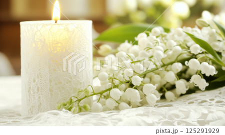 White ceremonial candle surrounded by delicate lilies of the valley flowers, symbol of christening 125291929