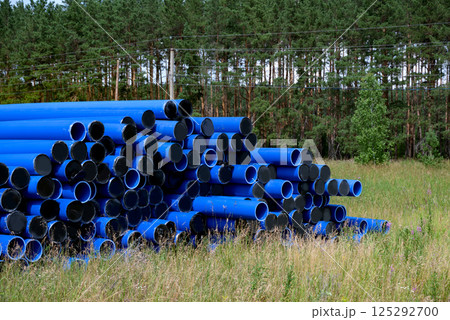 Stacked blue pipes resting in a field near a forest during daylight Stacked blue pipes resting in a field near a forest during daylight 125292700