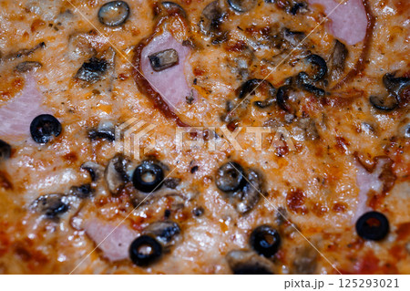 Delicious close-up of a pizza with ham, mushrooms and black olives on melted cheese, showcasing vibrant colors and appetizing texture 125293021