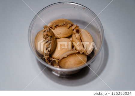 Heap of traditional fortune cookies with nut filling inside clear plastic container, top-down view on a white surface 125293024