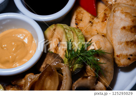 Grilled chicken breast served with avocado slices, mushrooms, sauces and fresh herbs on white plate close-up view Grilled chicken breast served with avocado slices, mushrooms, sauces and fresh herbs on white plate close-up view 125293029