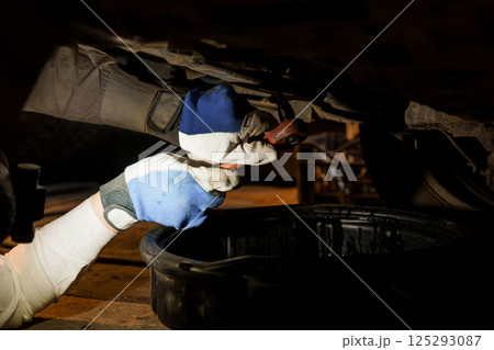 Mechanic Working Under Vehicle with Tools in Dim Lighting 125293087