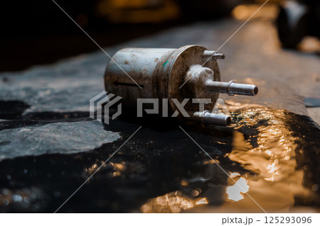 Industrial Fuel Filter Lying on a Wet Surface in a Dimly Lit Environment 125293096