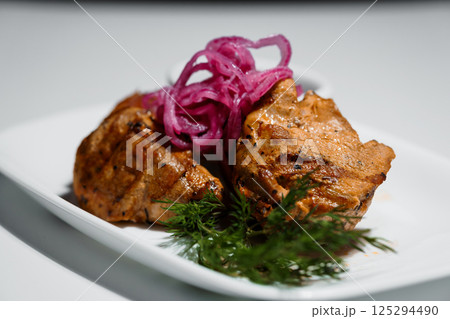 Grilled meat with pickled red onions and fresh dill served on a white rectangular plate, close-up studio shot Grilled meat with pickled red onions and fresh dill served on a white rectangular plate, close-up studio shot 125294490