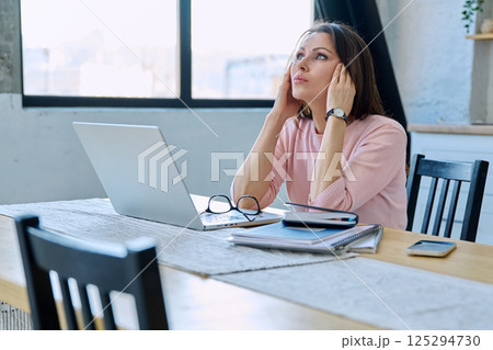 Middle aged sad stressed woman sitting at home at table with computer 125294730