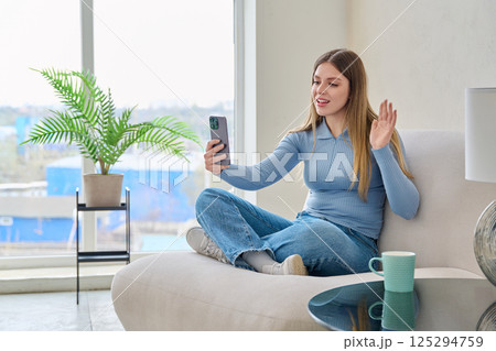 Young woman sitting at home in chair using smartphone, having video chat 125294759