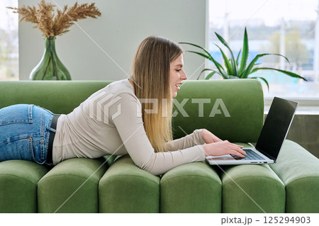 Young woman lying on sofa at home using laptop Young woman lying on sofa at home using laptop 125294903