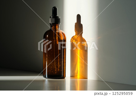 A bottle of serum made of brown glass on a white background with stripe of light. 125295059