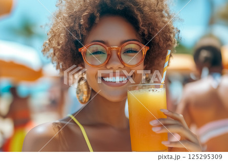 Smiling african american girl in round glasses enjoys refreshing orange juice on sunny beach day in tropical paradise with colorful umbrellas 125295309