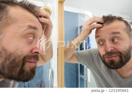 Happy adult man looking at hair in mirror 125295661
