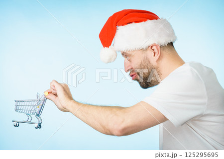 Man in santa hat holds empty shopping cart Man in santa hat holds empty shopping cart 125295695
