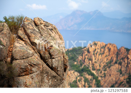 A rugged coastal rock formation set against a backdrop of mountains 125297588