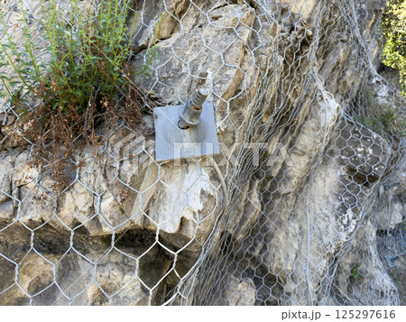 Steel mesh and anchor bolts fixed to rocky mountain surface. Engineering solution for slope stability and rockfall prevention used in high risk geological areas Steel mesh and anchor bolts fixed to rocky mountain surface. Engineering solution for slope stability and rockfall prevention used in high risk geological areas 125297616
