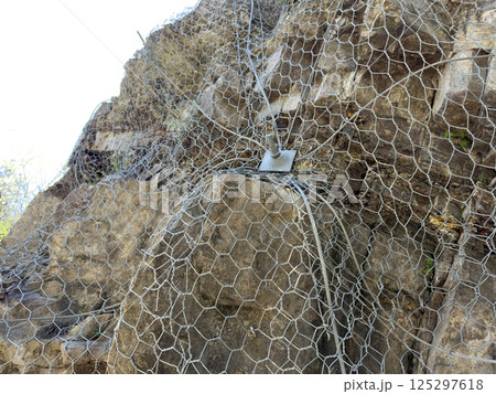 Protective mesh system installed on unstable rock slope to prevent rockfalls and minimize geological hazards. Essential safety measure in landslide prone areas. Protection against mountain collapse 125297618