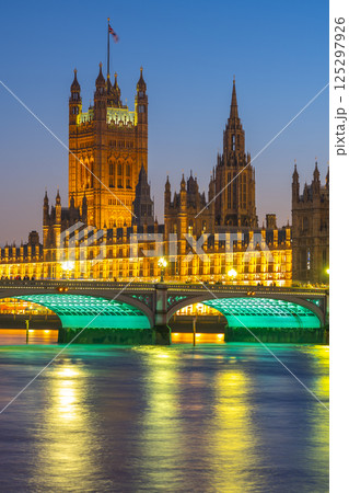 Westminster Palace stands illuminated against the twilight sky, reflecting on the Thames River. The glow of the buildings and bridge adds charm to this iconic location at dusk. Westminster Palace stands illuminated against the twilight sky, reflecting on the Thames River. The glow of the buildings and bridge adds charm to this iconic location at dusk. 125297926