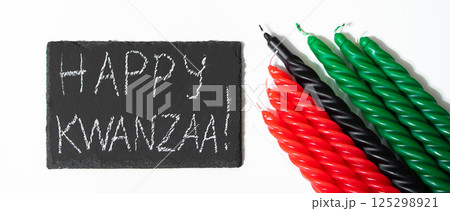 Happy Kwanzaa concept. Afro-American holiday. Congratulatory lettering and seven candles - red, black and green. African heritage symbol on white background. Happy Kwanzaa concept. Afro-American holiday. Congratulatory lettering and seven candles - red, black and green. African heritage symbol on white background. 125298921