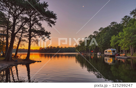 Lake with a sunset in the background and a small house on the shore. The water is calm and peaceful 125299247