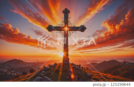 Large cross is lit up by the sun at sunset. The scene is peaceful and serene, with the sun setting behind the mountains in the background 125299644