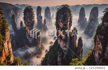 Mountain range with a foggy atmosphere. The mountains are tall and rocky, and the trees are lush and green. The sky is a mix of blue and pink, creating a serene and peaceful mood 125299891