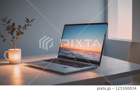 Laptop is open on a table with a vase of flowers next to it. The laptop screen shows a beautiful sunset with clouds in the sky. Concept of relaxation and tranquility 125300034