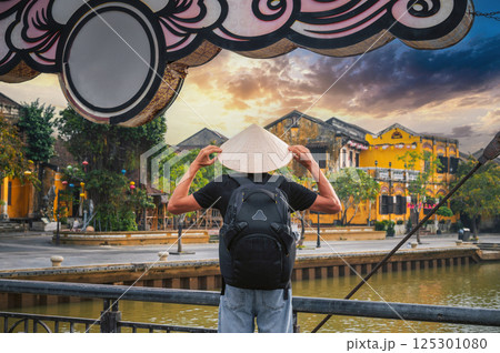 back of male tourist traveler in Vietnamese hat on bridge in old town in Hoi An in Vietnam in Asia 125301080