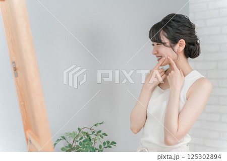 ニキビ・肌荒れ・吹き出物が治って笑顔で鏡を見るアジア人女性 ニキビ・肌荒れ・吹き出物が治って笑顔で鏡を見るアジア人女性 125302894