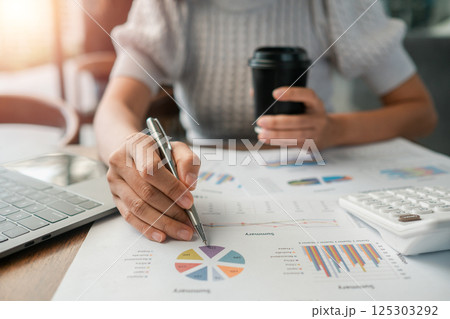 Close-up of a person reviewing financial charts with a laptop, calculator, and coffee in a modern office environment. 125303292