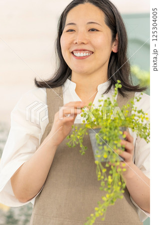室内で植物の世話をする笑顔の大人女性｜健康的な暮らしイメージ｜ウェルビー女子｜ウェルビーイング 125304005