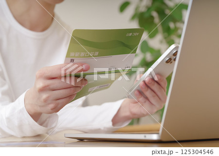 通帳とスマホで金銭のやり取りをする女性 通帳とスマホで金銭のやり取りをする女性 125304546