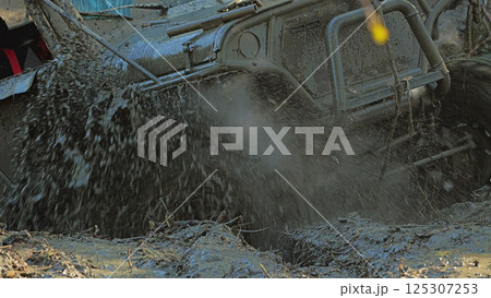 A muddy SUV whizzes through a deep puddle, creating a cloud of spray. Off-road competition in severe off-road conditions 125307253