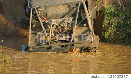 Close-up of the rear part of an SUV stuck in a muddy ditch. The vehicle is partially submerged in mud, the cooling system and the safety cage are visible 125307287